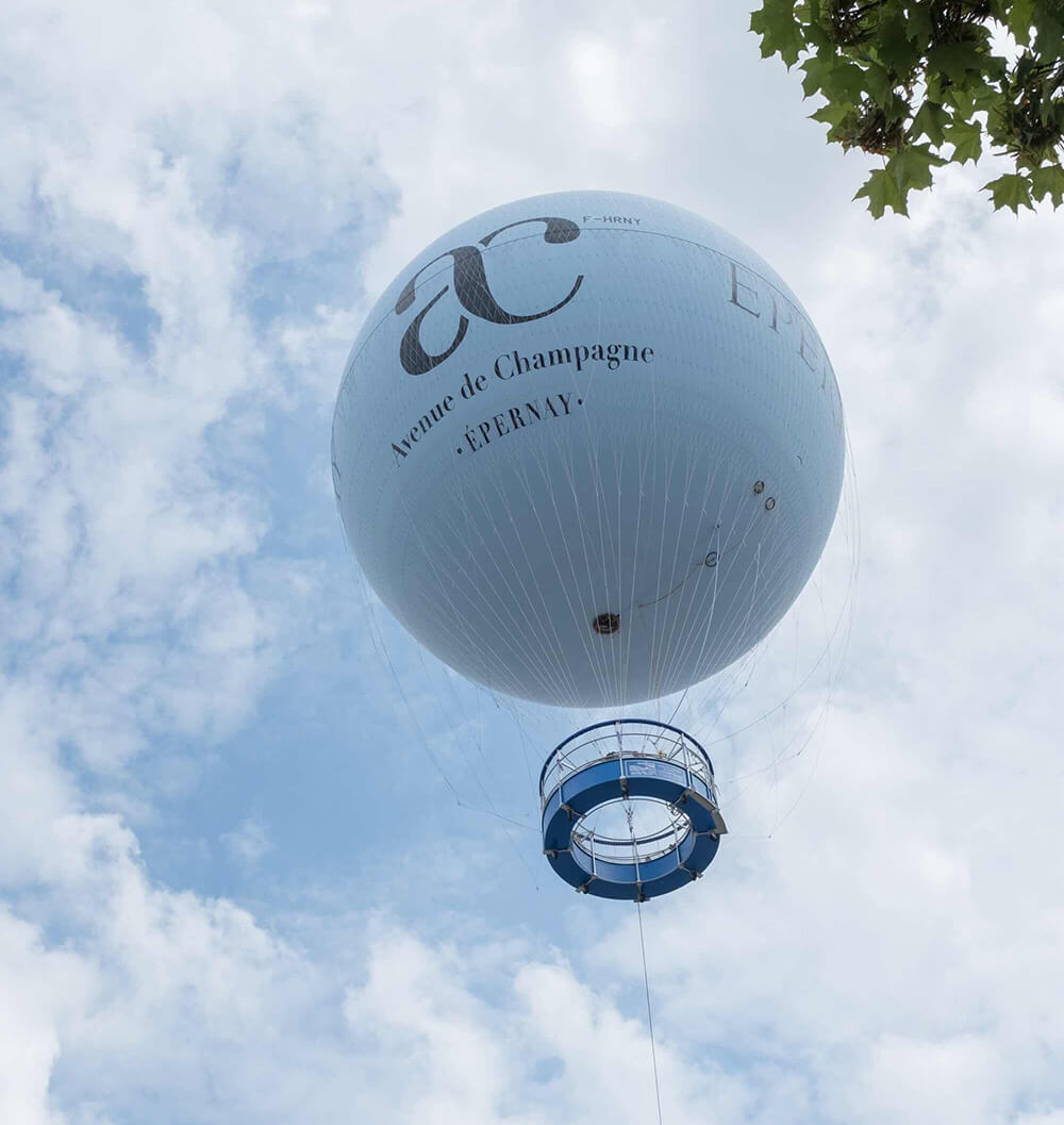 We see the light blue tethered Epernay balloon, in the cloudy blue sky, with its gondola.