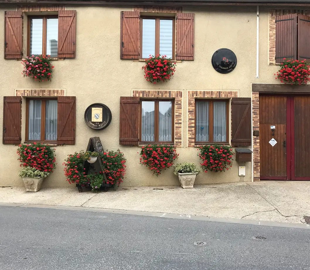 We see the beige facade of the Champagne TH. THOMAS-HATTE family estate, decorated with red floral hangings under the windows.