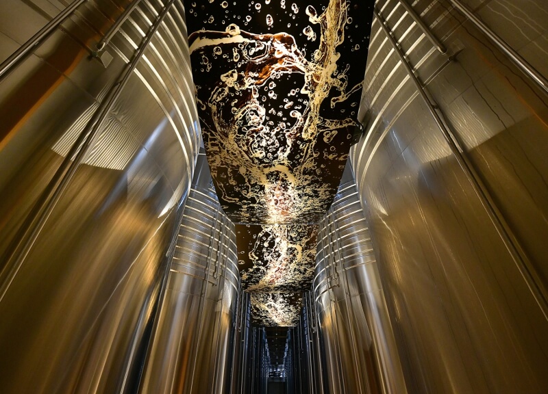 We can see part of the tour of the Nicolas Feuillatte cellars in a room with large silver vats, with a black ceiling decorated with shapes representing Champagne bubbles.