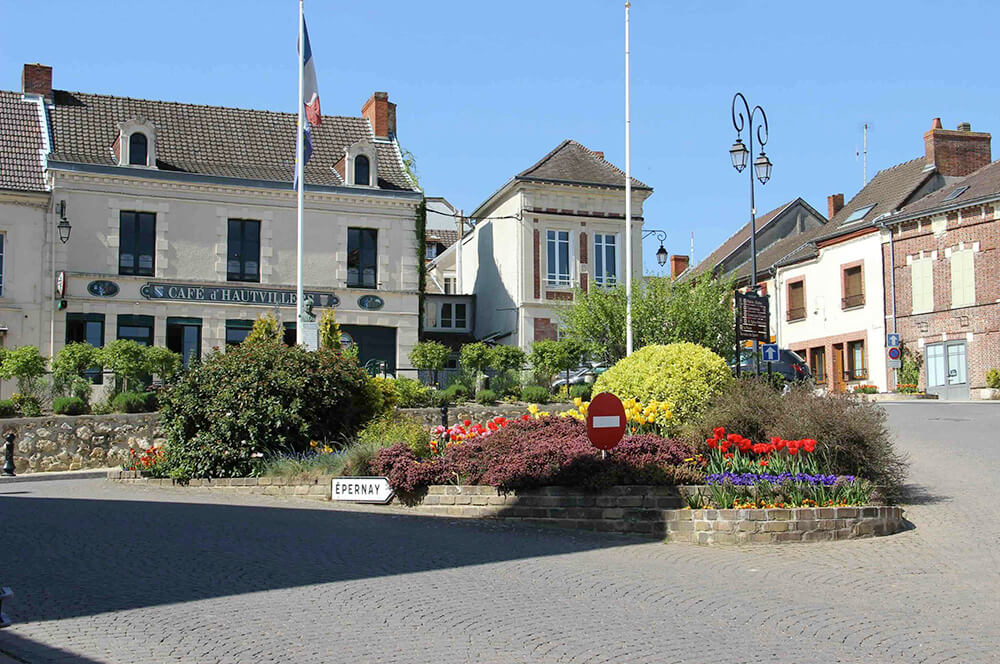 We see a cobbled street and a flowered square in front of the Hautvillers café.