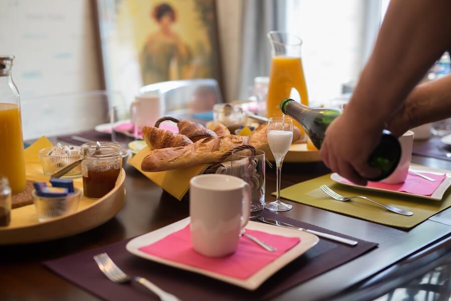 A close-up view of the breakfast table with baguettes, pastries, orange juice. Didier serves the glass of Champagne offered to the adults.